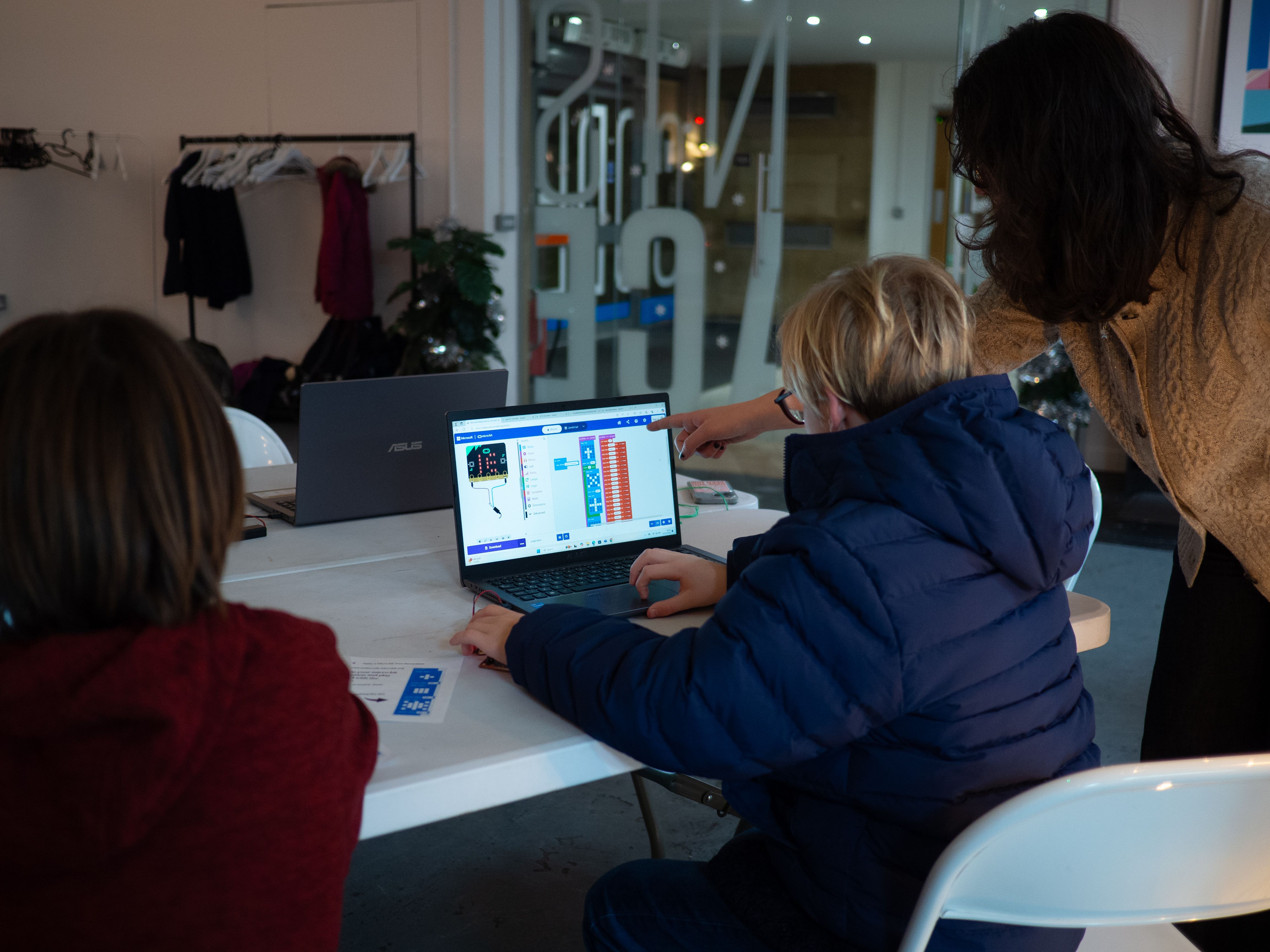 A young person programming a BBC micro:bit while a mentor is pointing at a screen